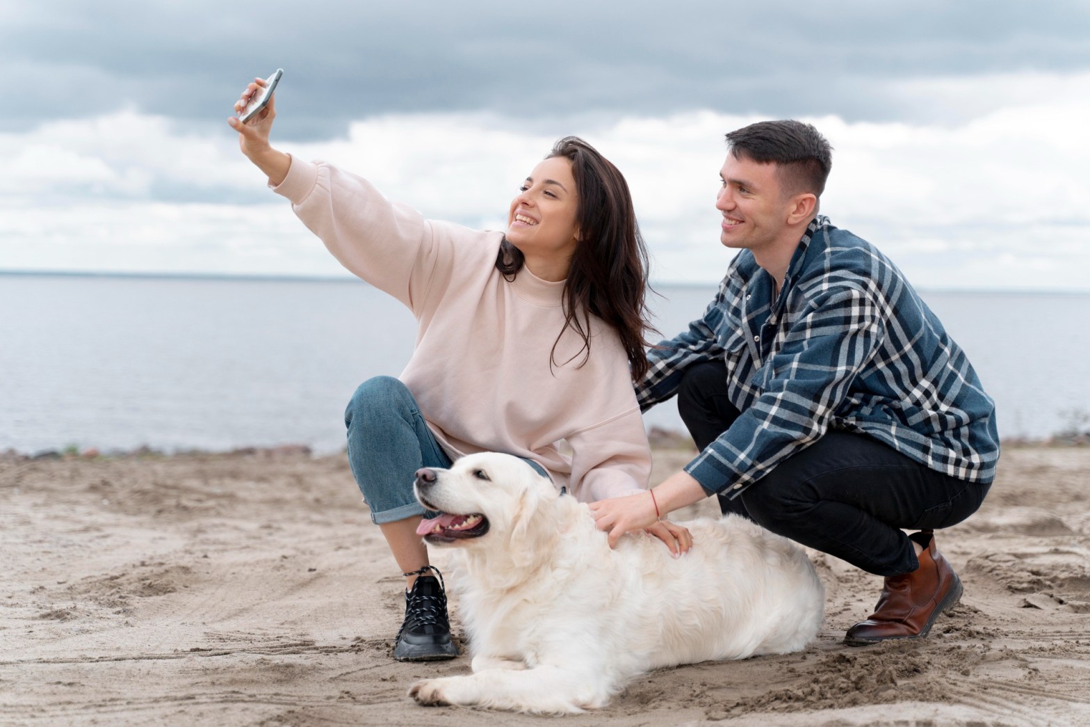 Pareja joven toma una selfie con su perro en la playa, representando el turismo pet friendly como experiencia emocional y tendencia en crecimiento