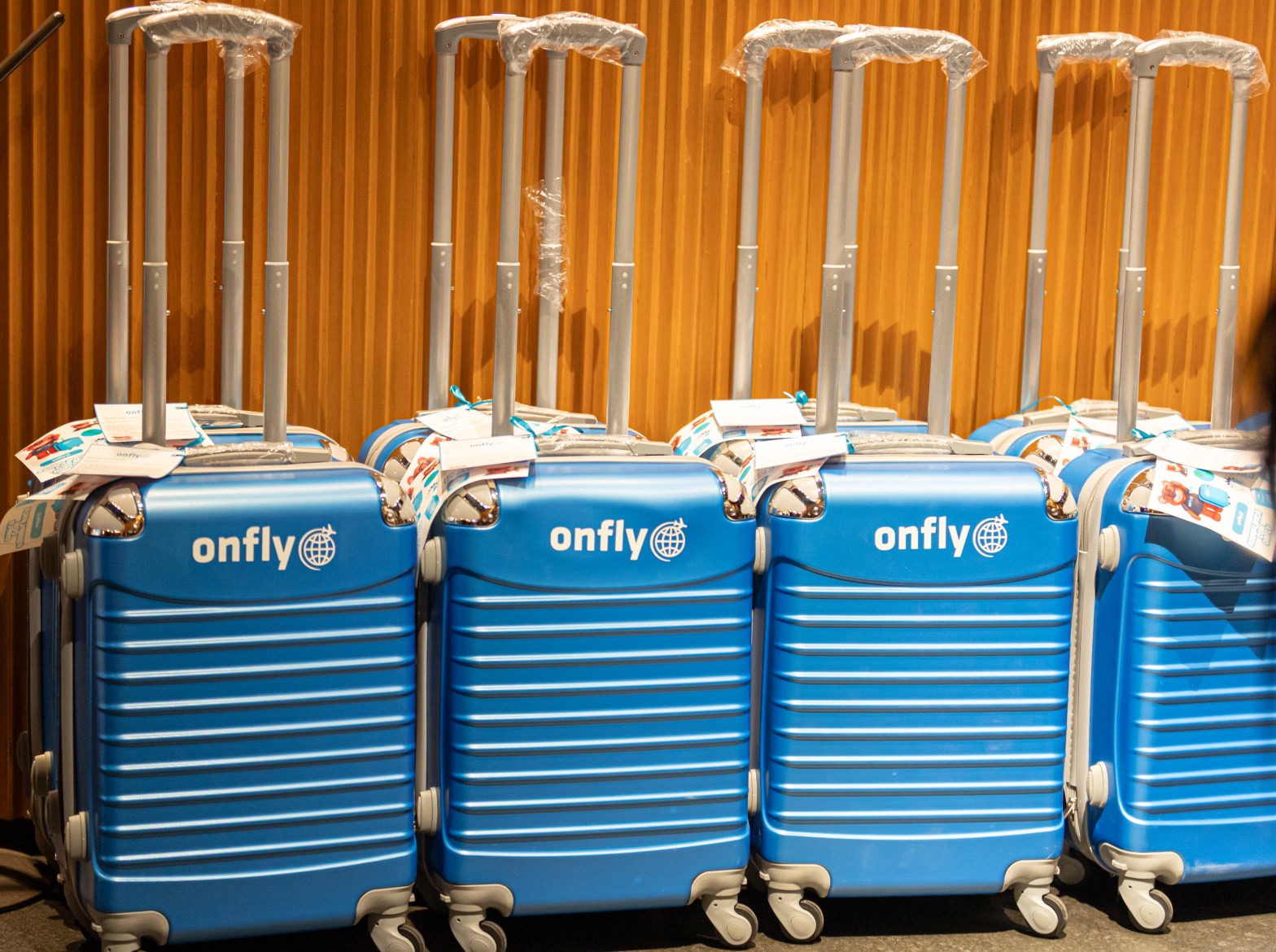 Fila de maletas azules con el logo de Onfly alineadas frente a una pared de madera durante un evento corporativo. La imagen simboliza el enfoque de la marca en los viajes de negocios, la conexión con el viajero moderno y su presencia estratégica en el mercado mexicano.