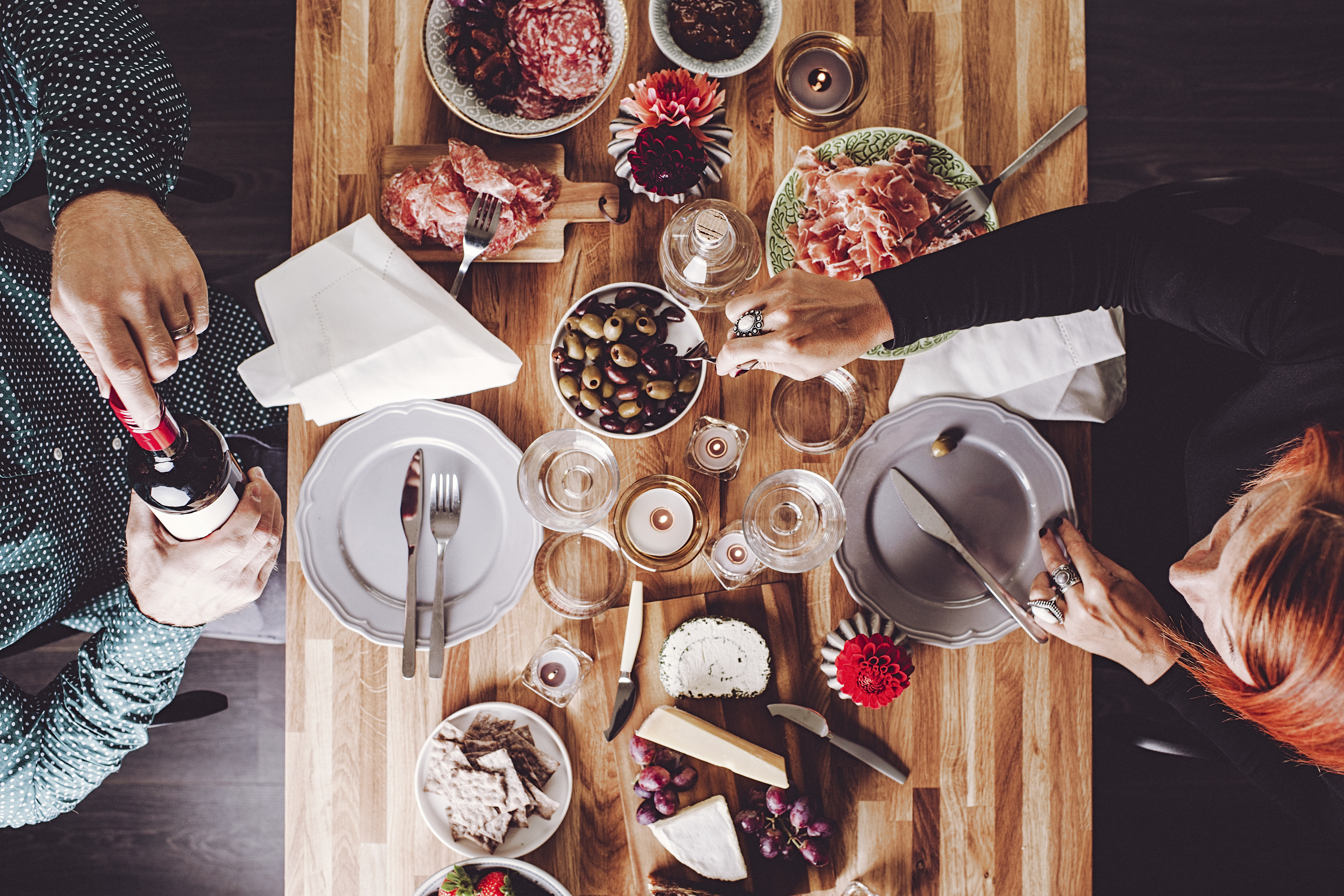 Vista cenital de una mesa servida con charcutería, quesos, aceitunas, vino y pan, mientras dos personas comparten el momento de manera íntima y sofisticada. La imagen transmite la esencia del sector HORECA, resaltando la importancia de la experiencia gastronómica como motor del turismo y la hospitalidad