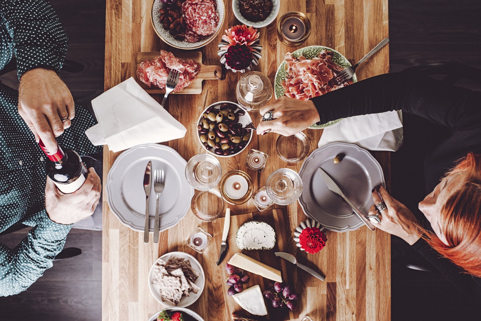 Vista cenital de una mesa servida con charcutería, quesos, aceitunas, vino y pan, mientras dos personas comparten el momento de manera íntima y sofisticada. La imagen transmite la esencia del sector HORECA, resaltando la importancia de la experiencia gastronómica como motor del turismo y la hospitalidad