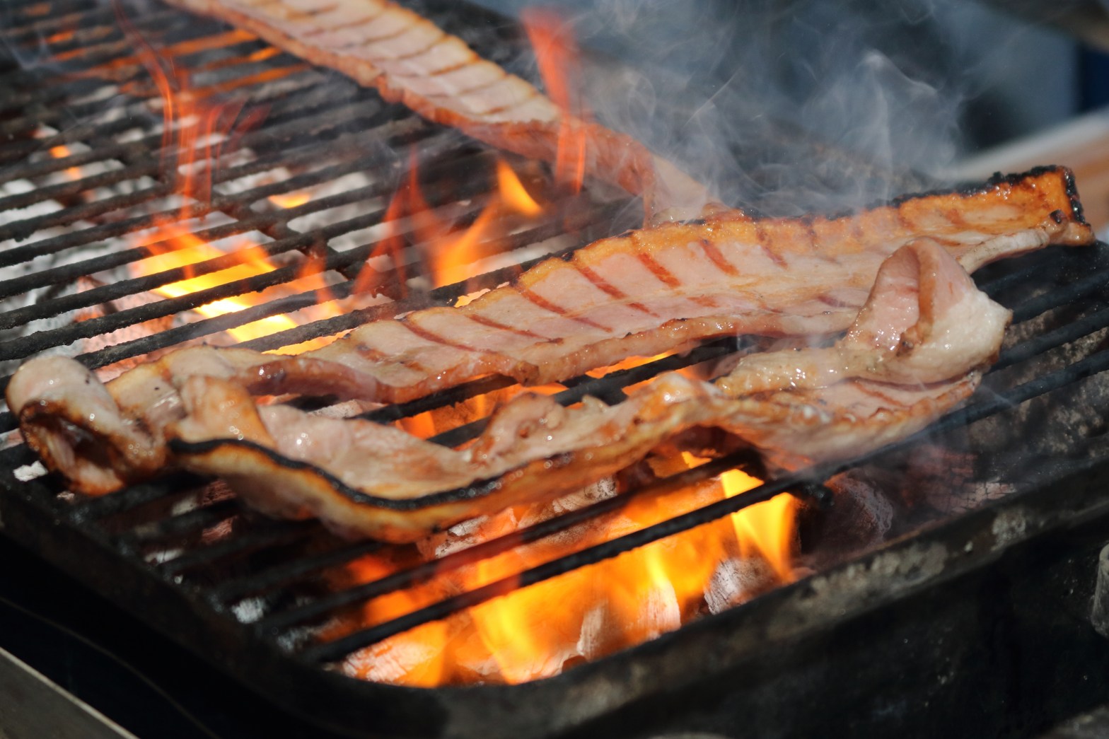 Carne sonorense asándose al fuego entre humo y brasas durante una experiencia gastronómica tradicional
