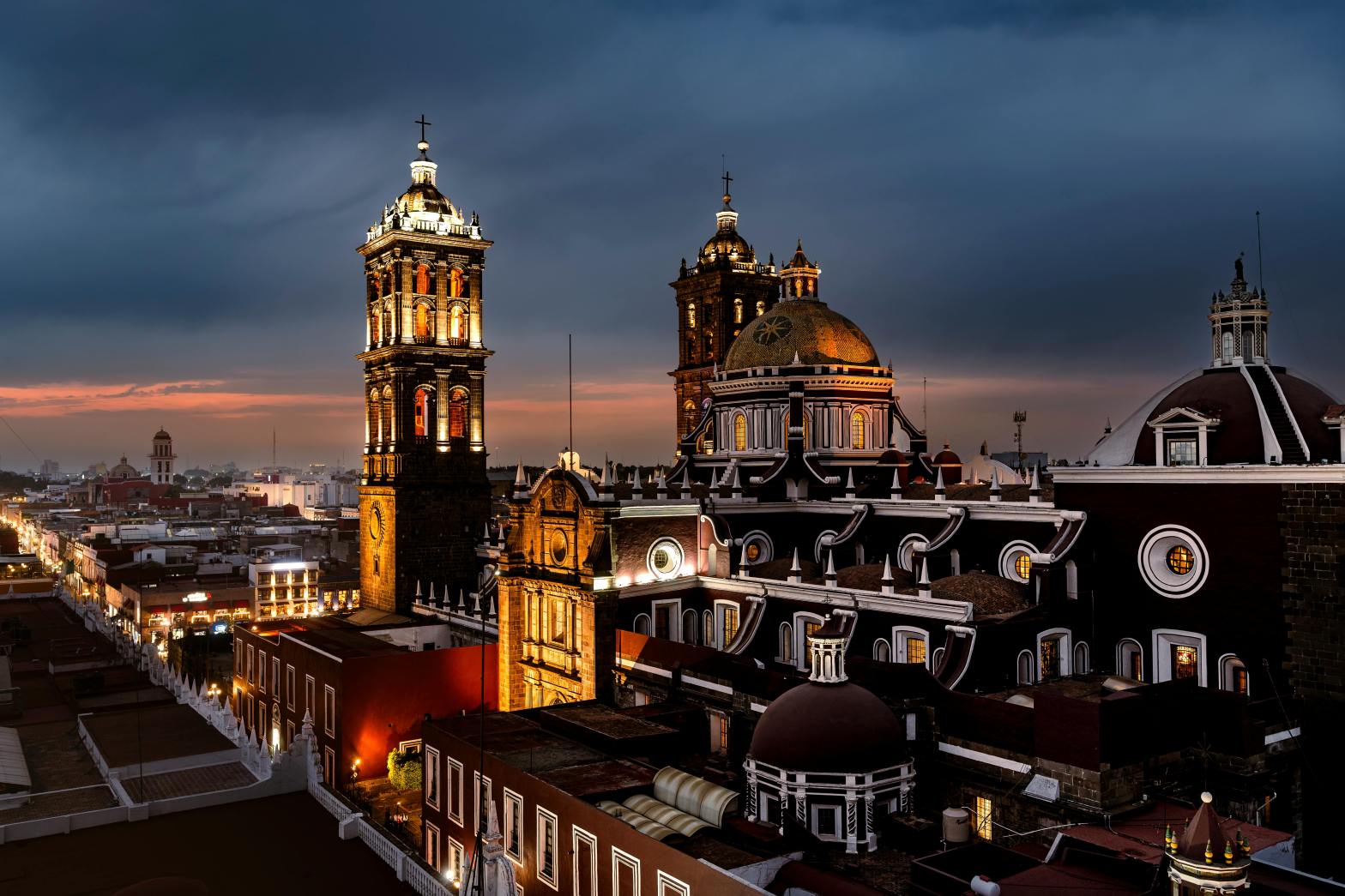 Vista nocturna del Centro Histórico de Puebla iluminado, con la Catedral de Puebla y arquitectura colonial bajo un cielo dramático