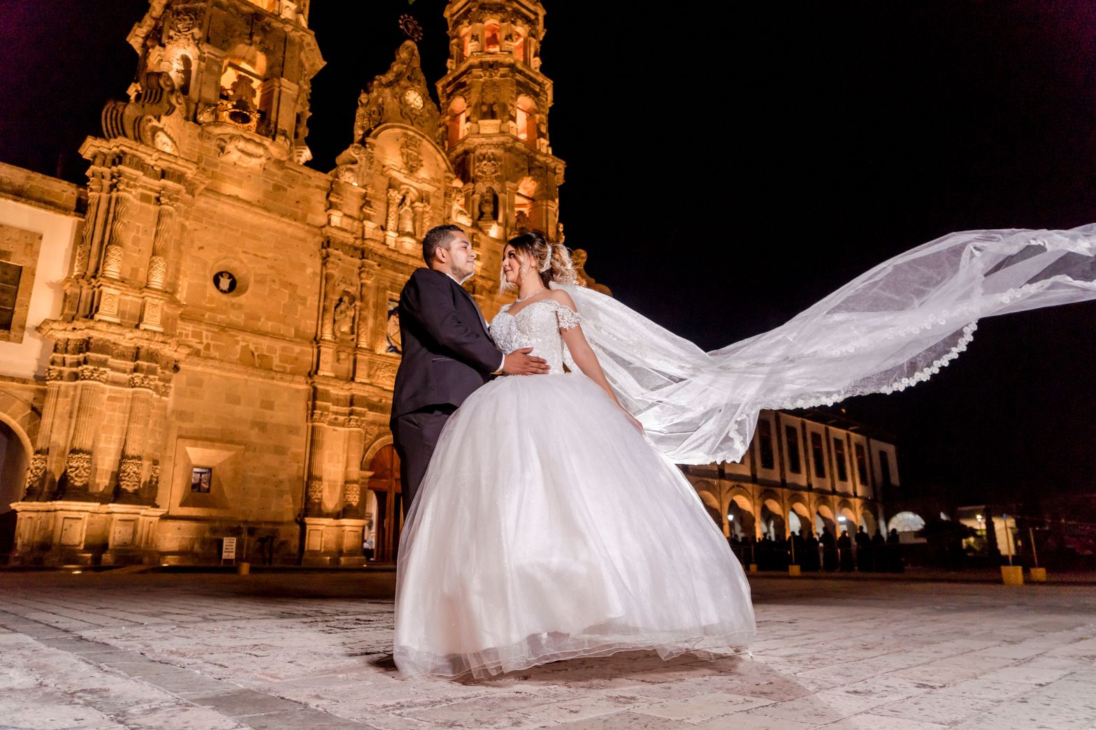 Pareja de recién casados posa frente a una catedral histórica iluminada, reflejando la conexión entre las Bodas Destino y la identidad cultural del lugar