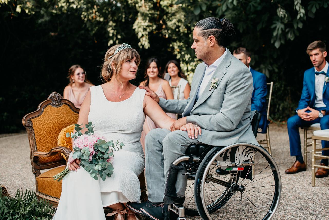 Pareja celebra su boda durante una ceremonia al aire libre; uno de los contrayentes utiliza una silla de ruedas, reflejando la importancia de la accesibilidad en el turismo de romance