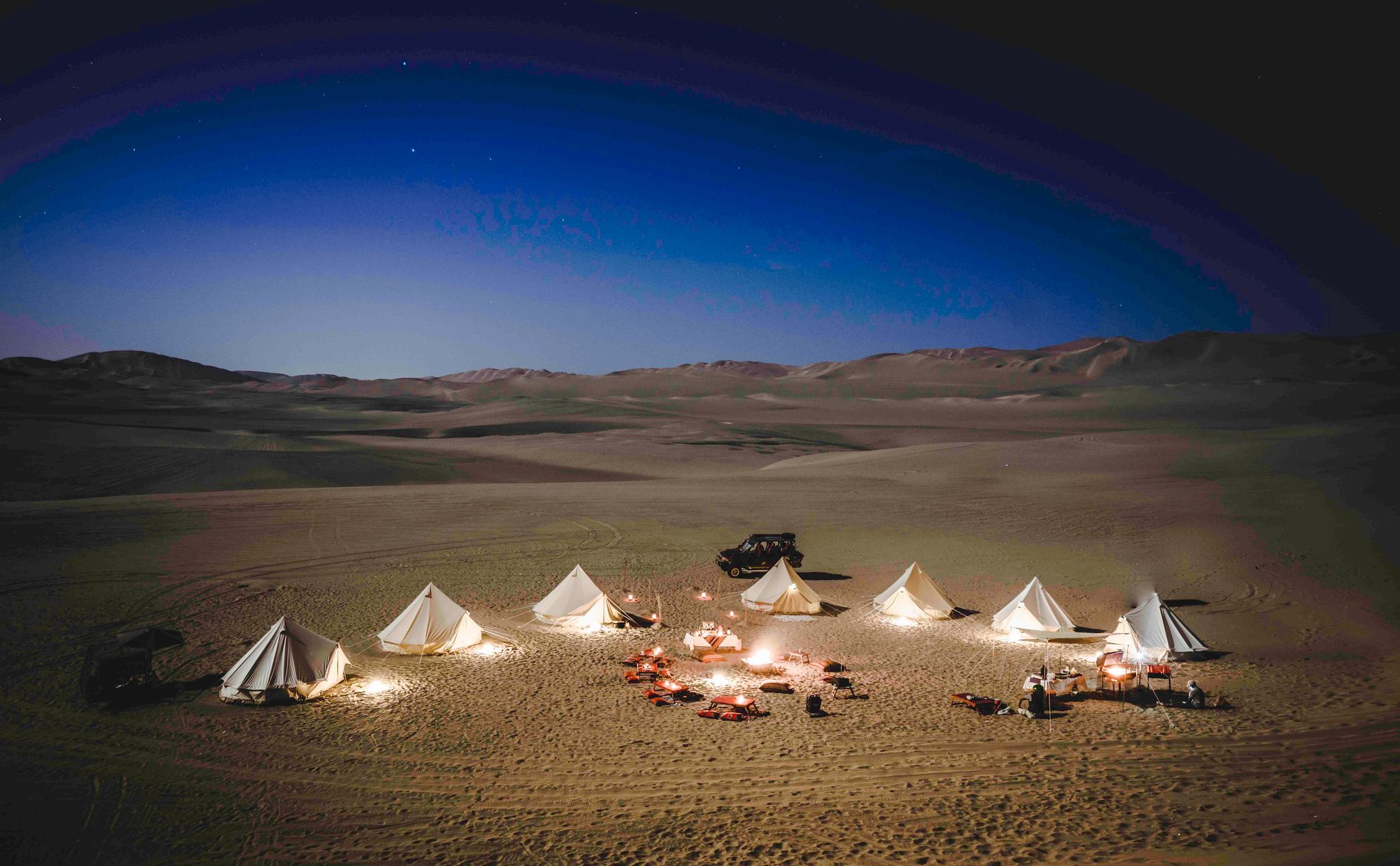 Campamento iluminado entre las dunas de Ica, Perú, durante una experiencia nocturna para grupos
